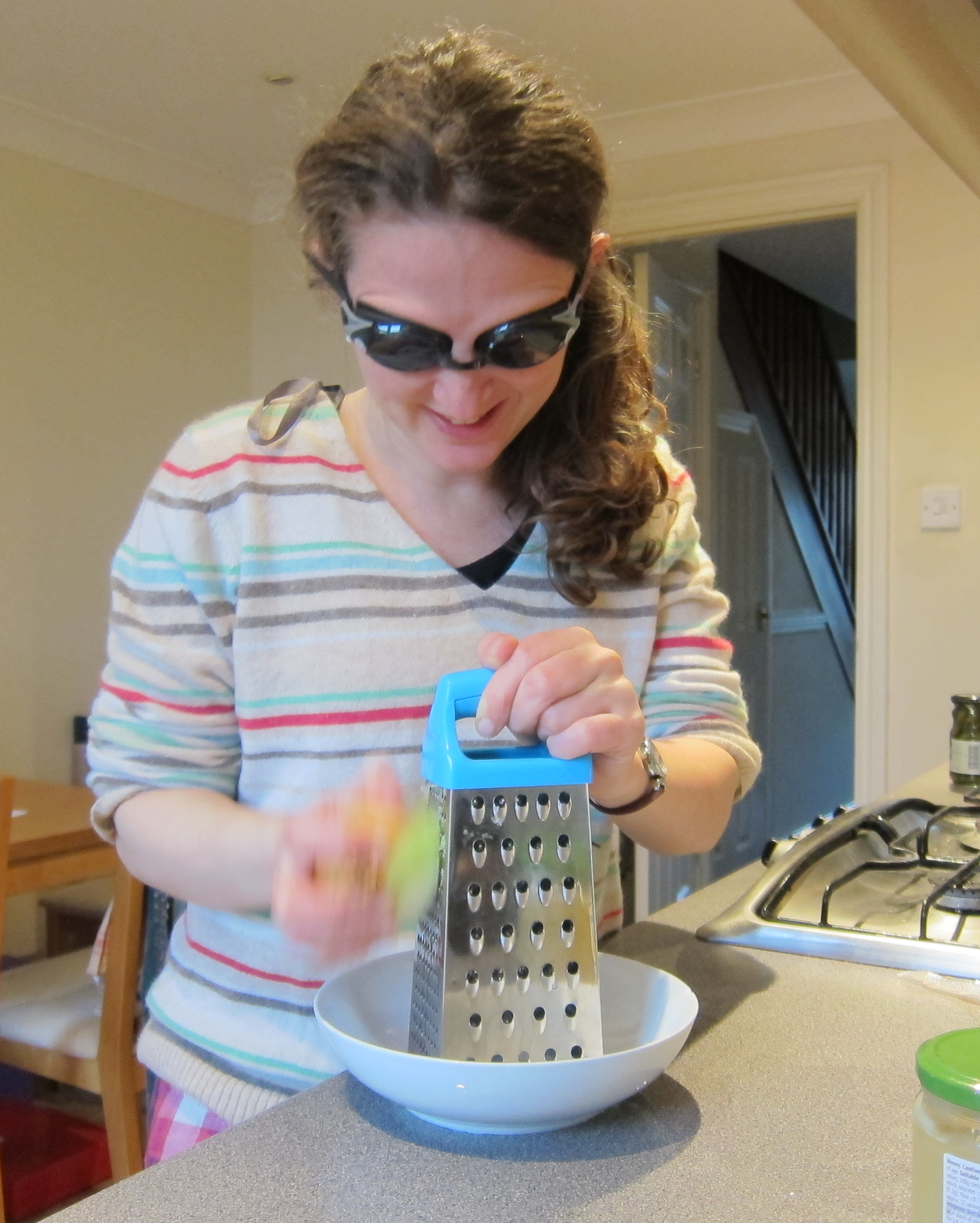 Dalya grating onions into a bowl while wearing goggles