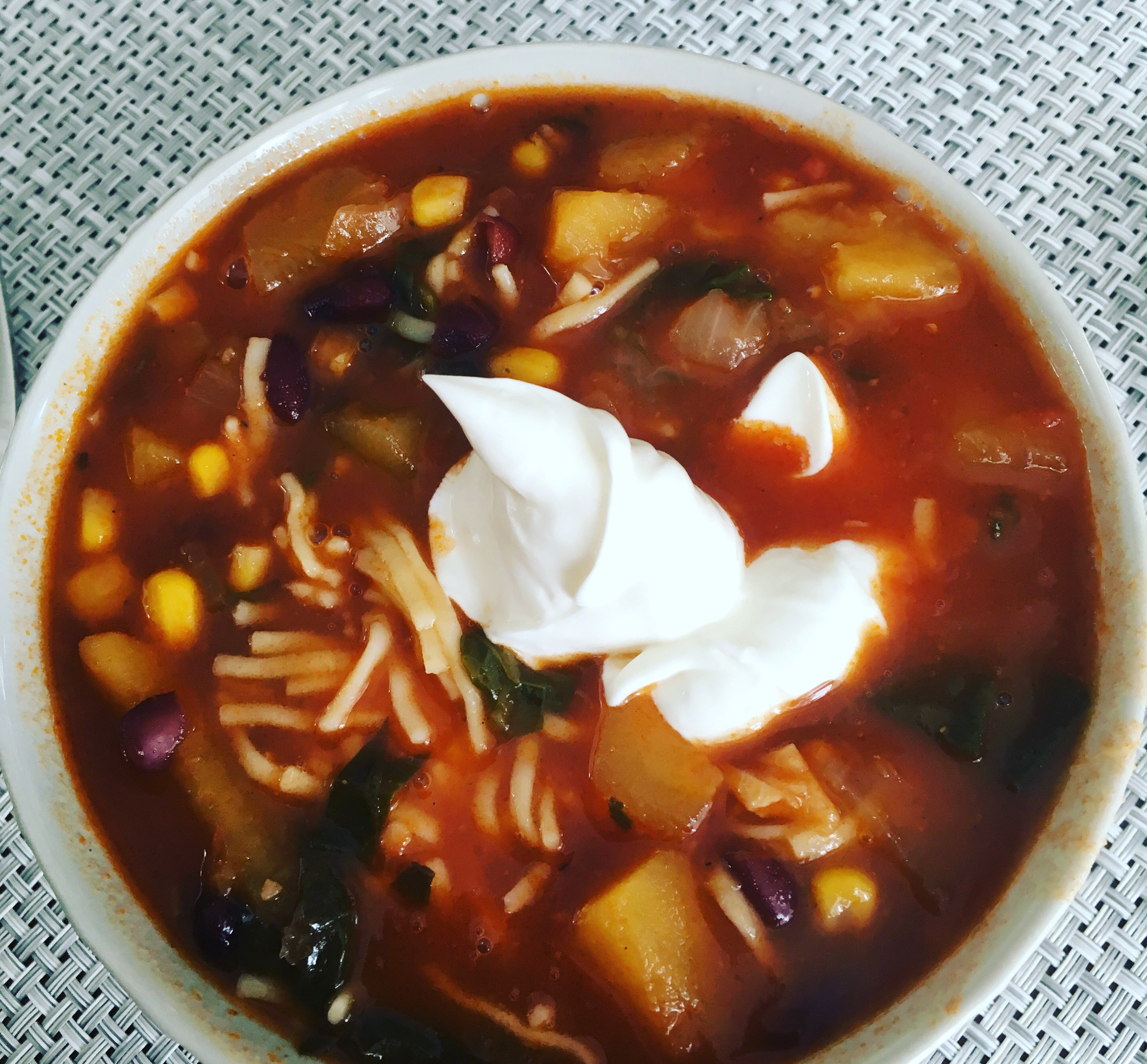 Soup with squash, beans, and noodles garnished with sour cream in a bowl