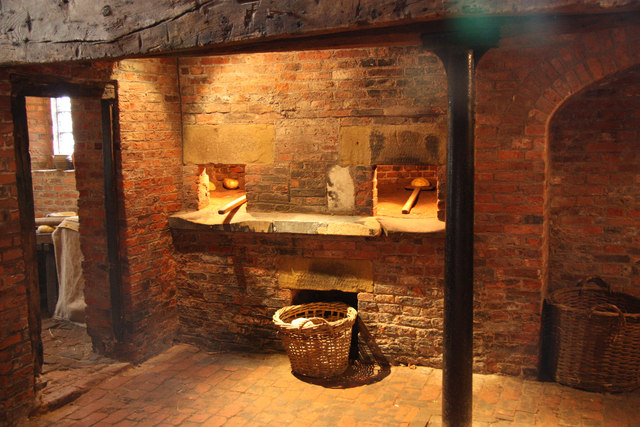 A medieval oven with two wooden sticks going into holes in a brick edifice, with a fire within
