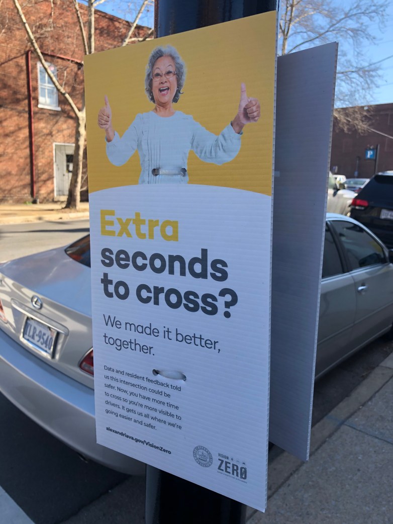 A sign with an Asian elder woman with thumbs up on a street pole, saying "Extra seconds to cross? We made it better together.